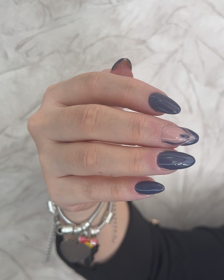 Mano con uñas largas en forma almendrada, esmaltadas en azul oscuro y una con diseño transparente decorado con líneas en el mismo tono.