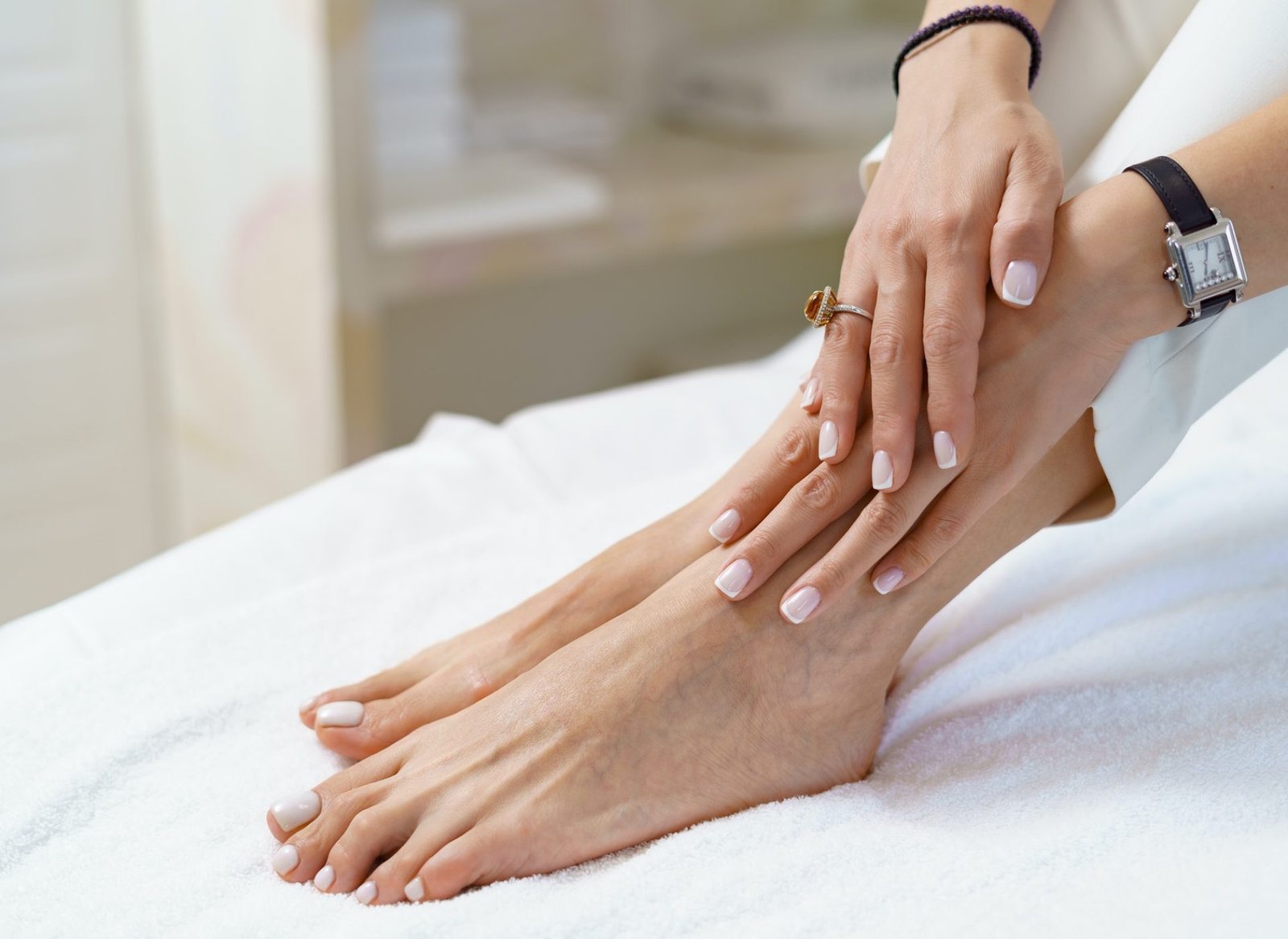 Primer plano de pies y manos femeninas reposando sobre una superficie blanca. Uñas de pies y manos están cuidadas y esmaltadas en color rosa claro.